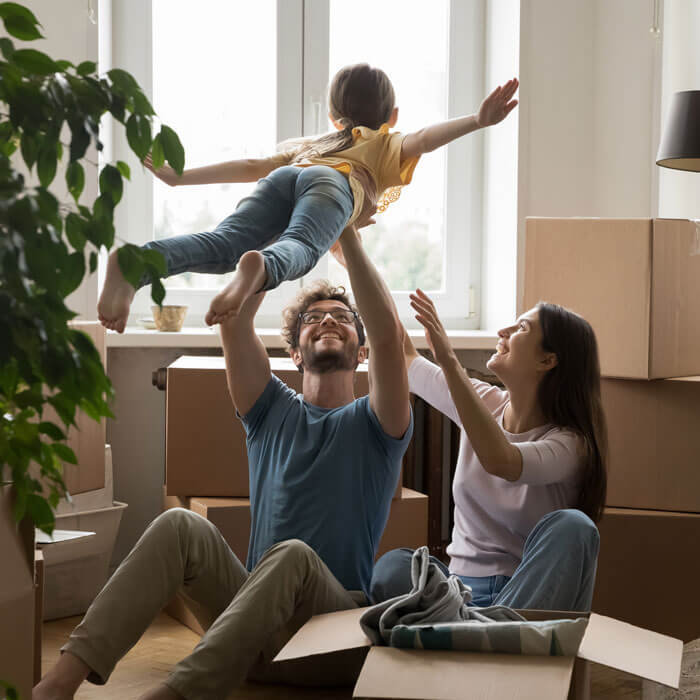 dad lifting daughter while sitting on floor of new home with mom in front of lots of moving boxes